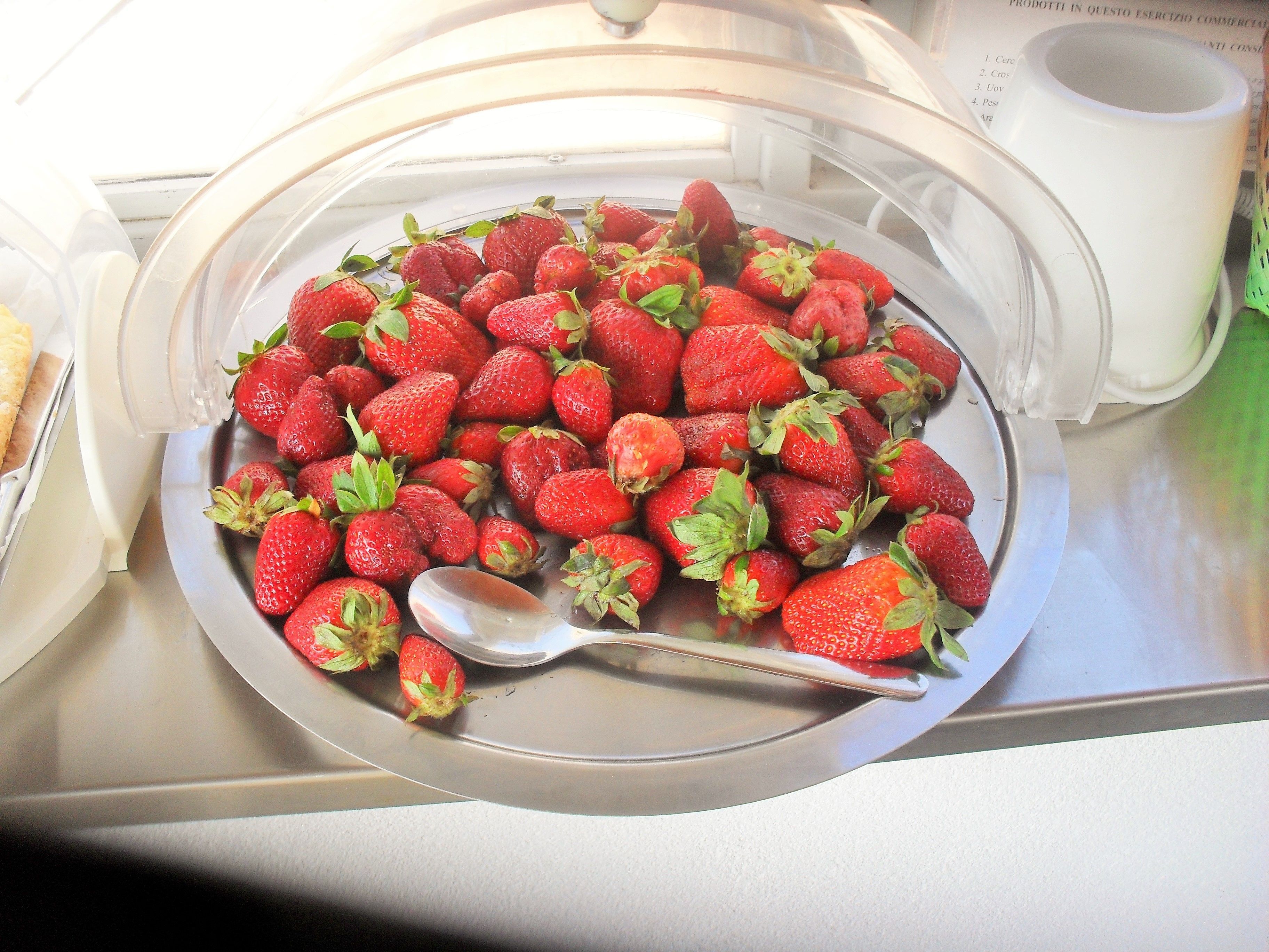 A bowl of strawberries with a spoon inside a microwave.