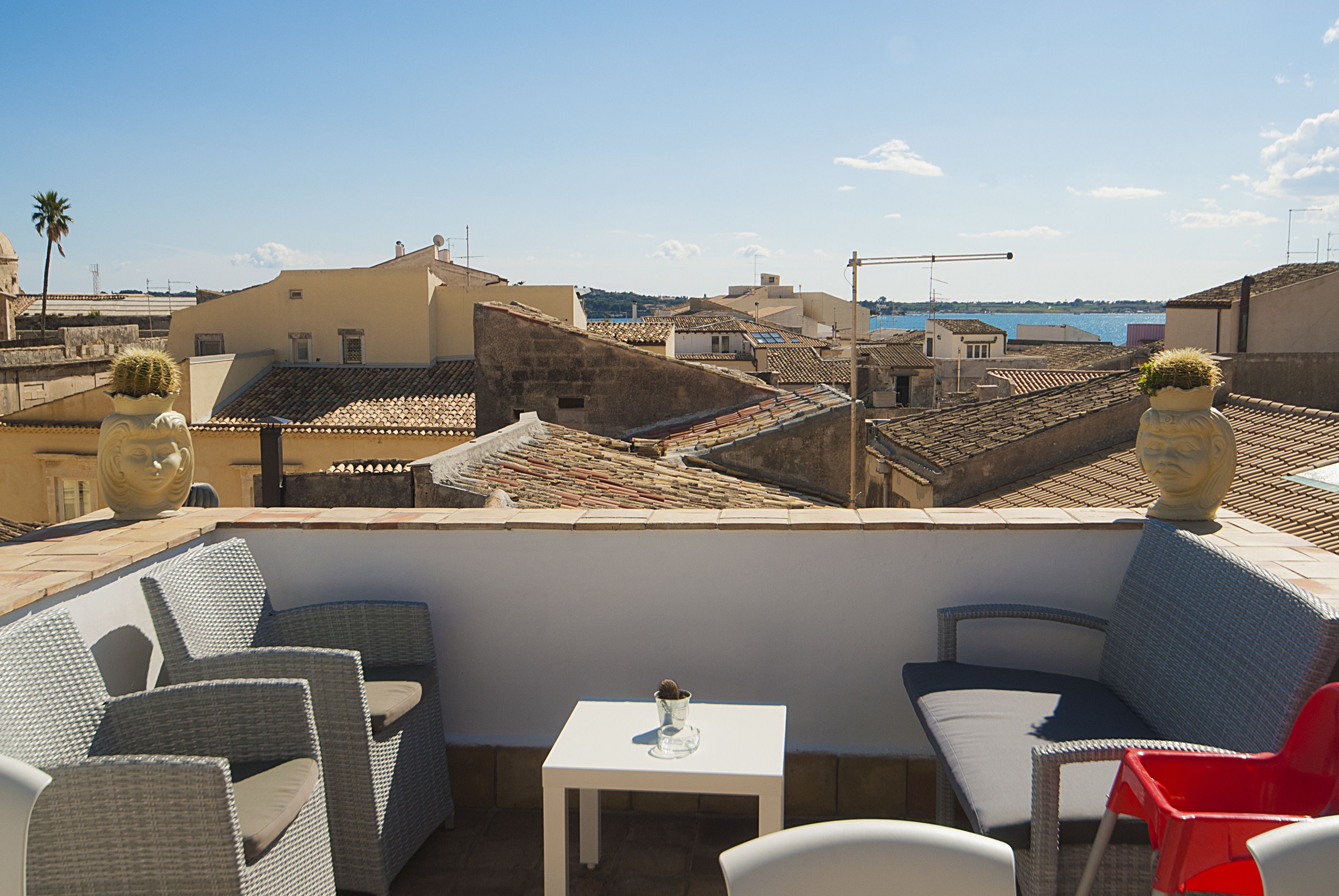 A rooftop terrace with wicker furniture, a small table, and decorative vases.