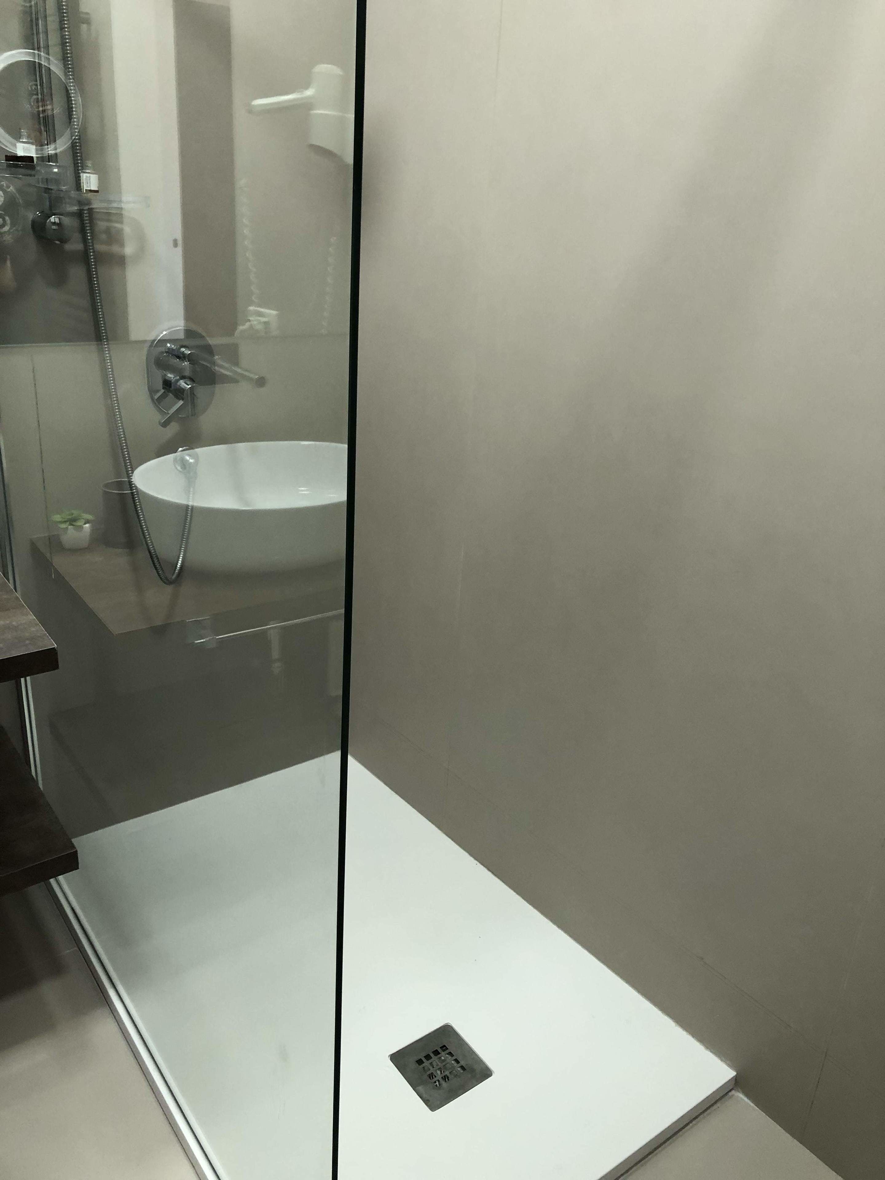Une salle de bain moderne avec une douche à l’italienne en verre, un lavabo blanc et un drain apparent.