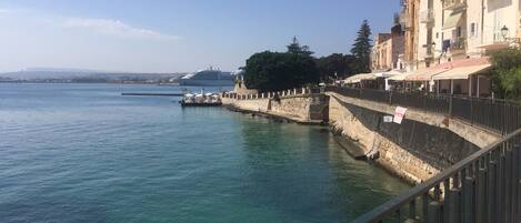 A coastal scene with a stone wall, a pier, and a cruise ship in the distance.