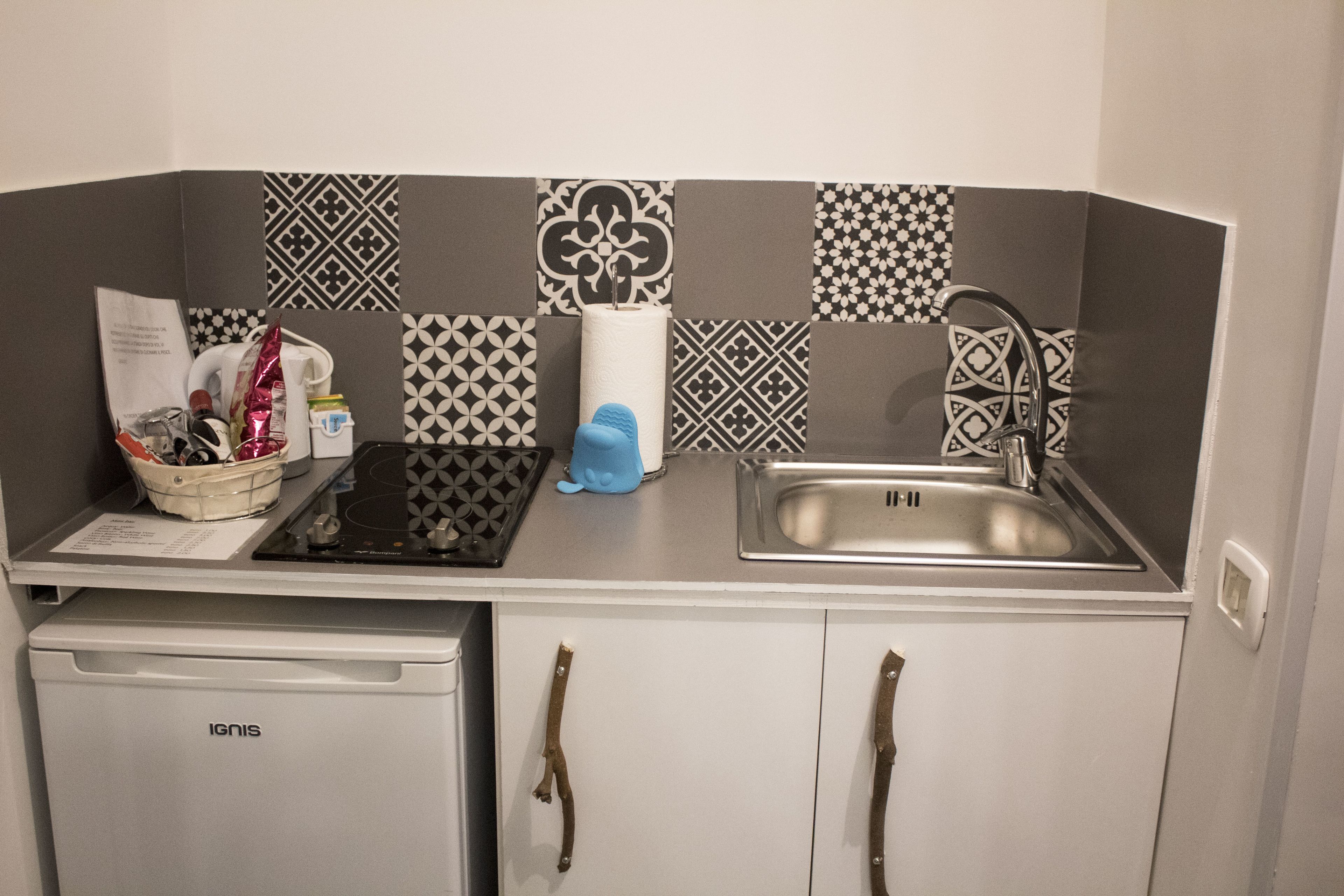 Una kitchenette compacta con un lavamanos, un refrigerador pequeño y un salpicadero con diseño.