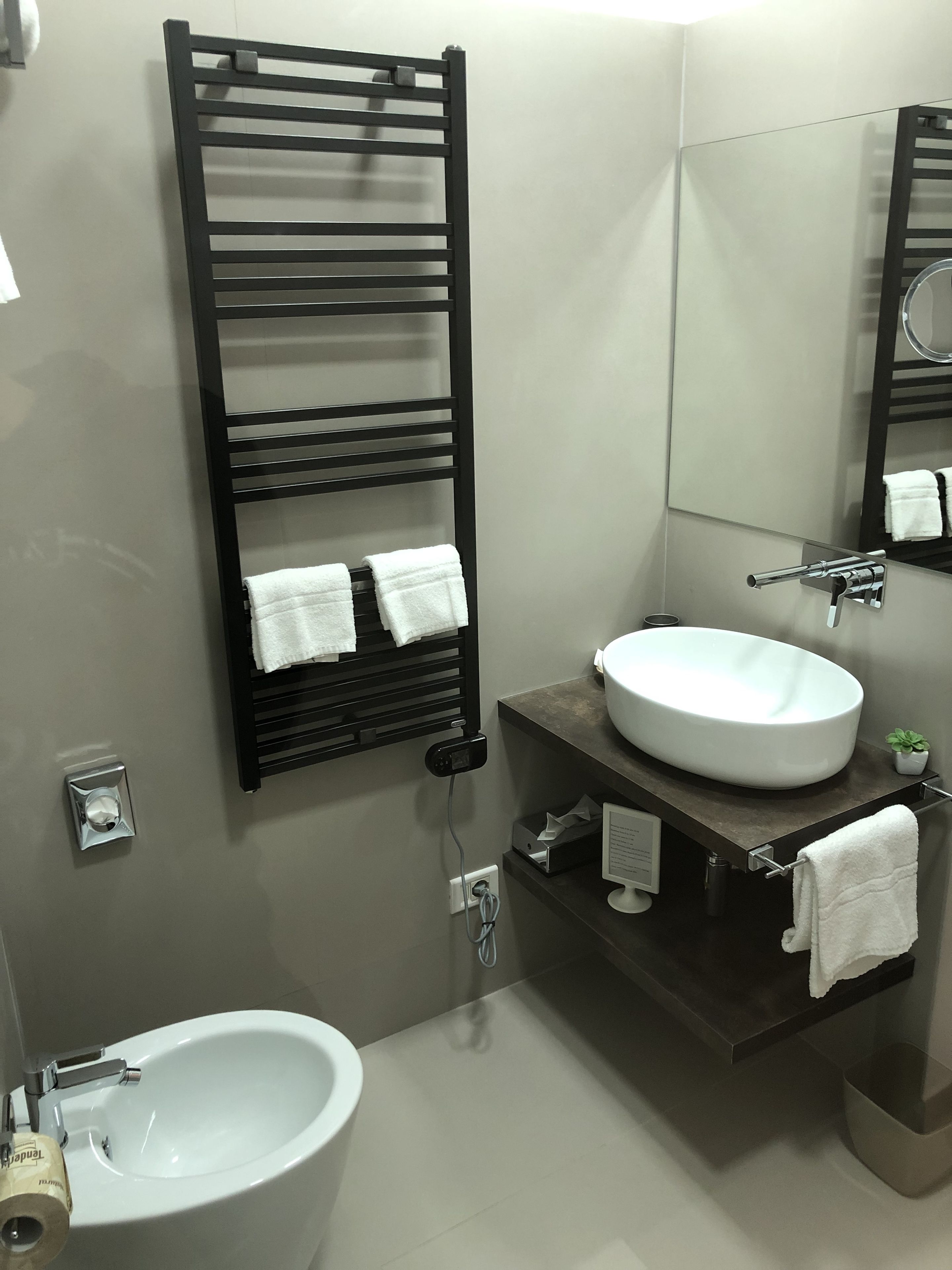 Een moderne badkamer met een zwarte handdoekhouder, een witte wastafel en een spiegel.