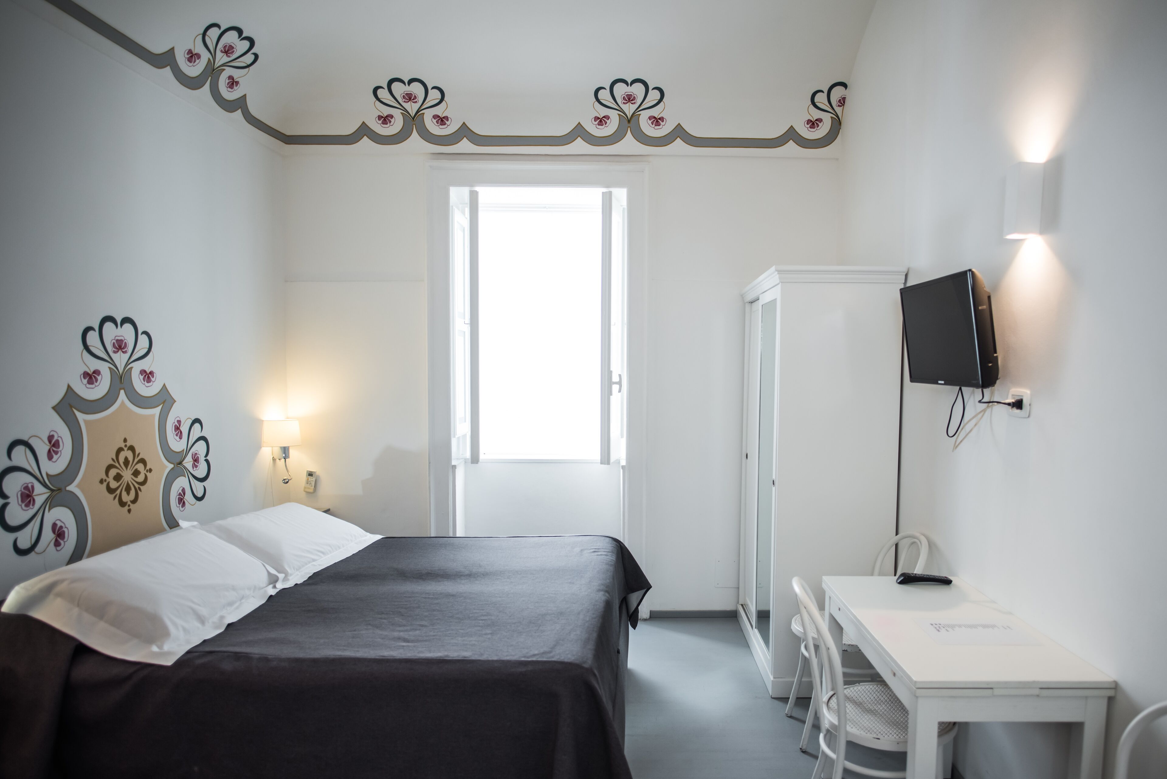 A bedroom with a bed, bedside table, TV, and a desk with chairs.