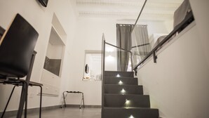A staircase with a glass railing, a chair, and a small table with a lamp. - Aretusa Vacanze B&B (Syracuse)