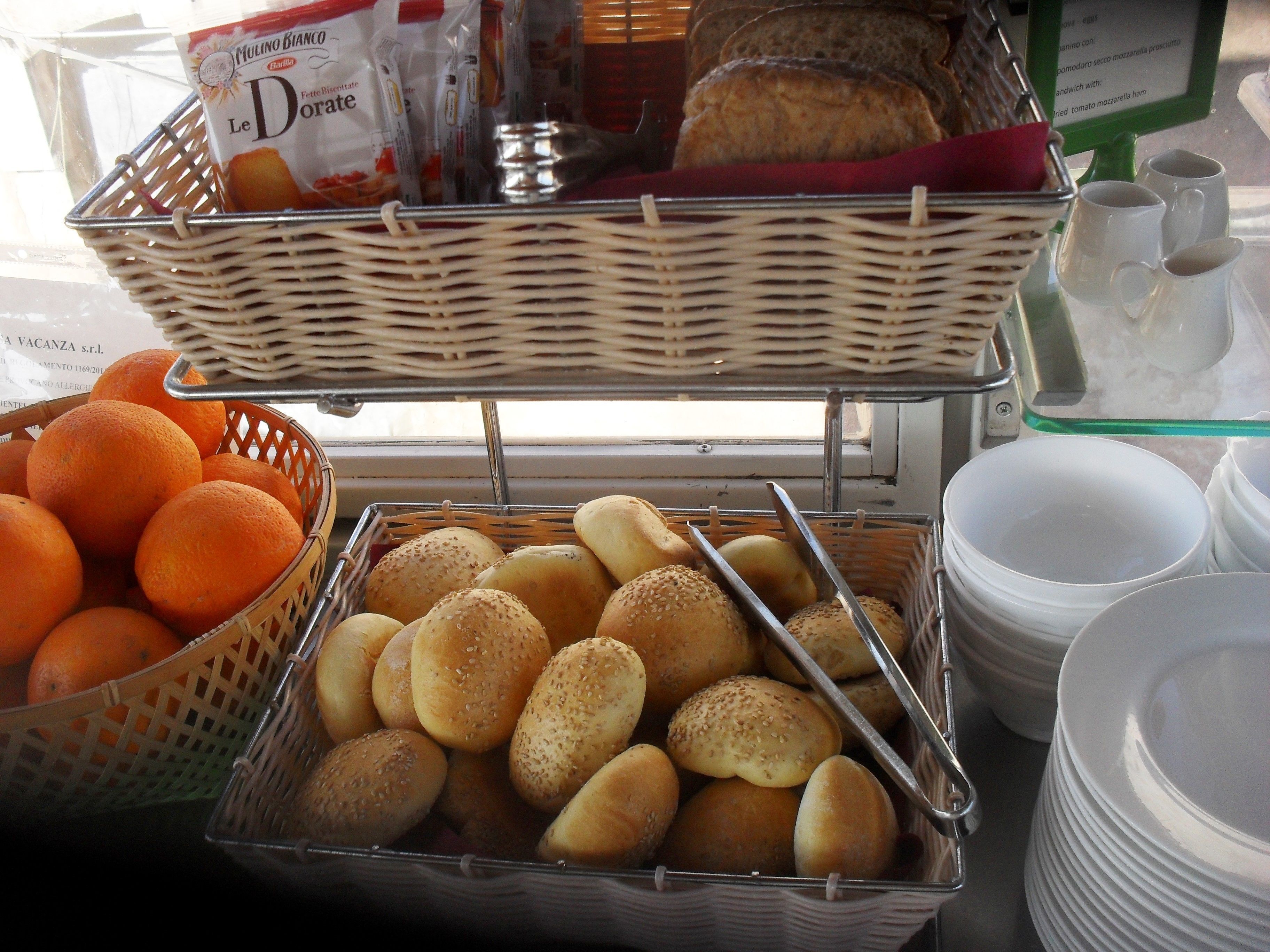 Een buffetopstelling met broedjes in manden en sinaasappels, plus een pak koekjes.