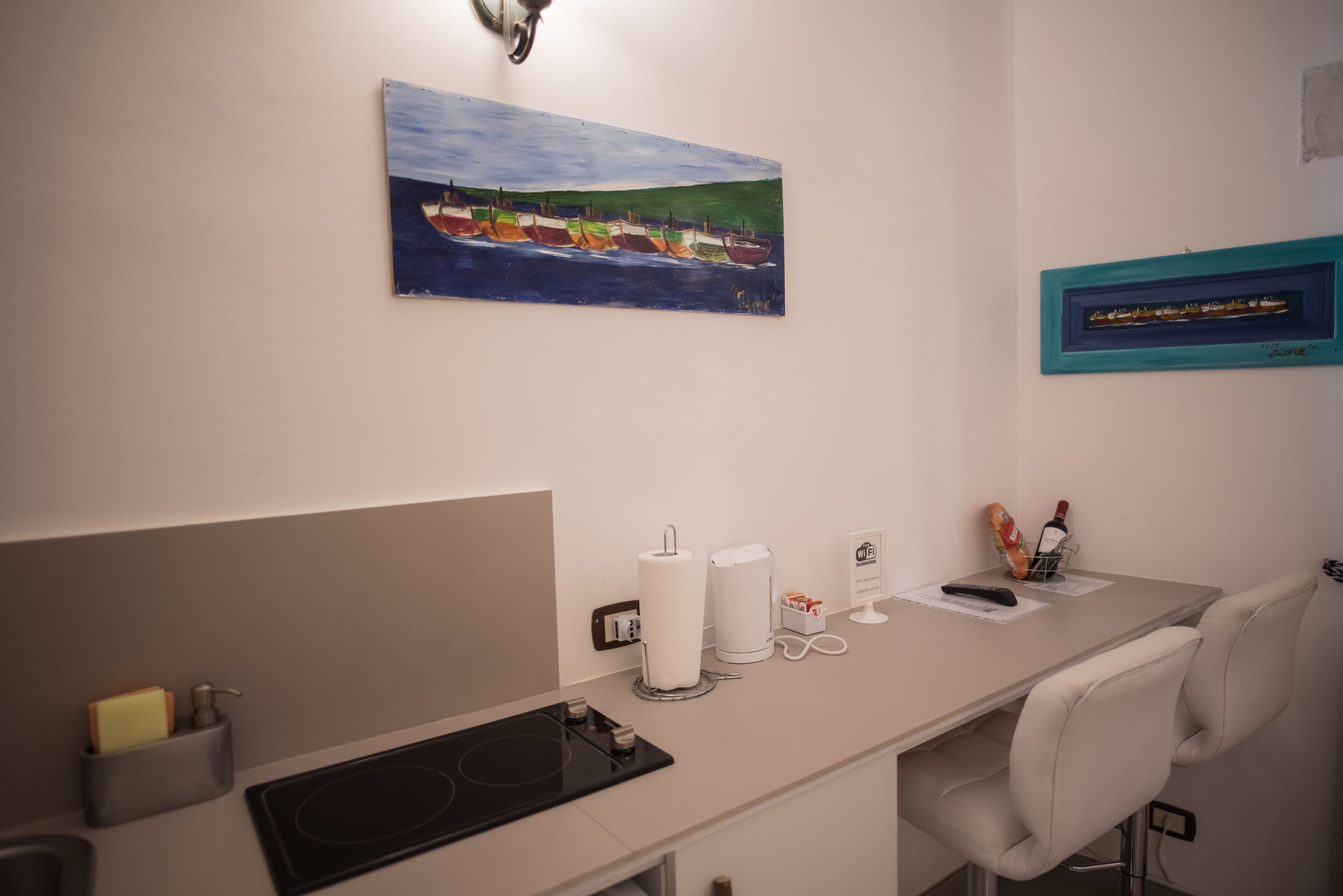 Una cocina moderna con encimera blanca, un cuadro de barcos en la pared y una fotografía con marco verde azulado.