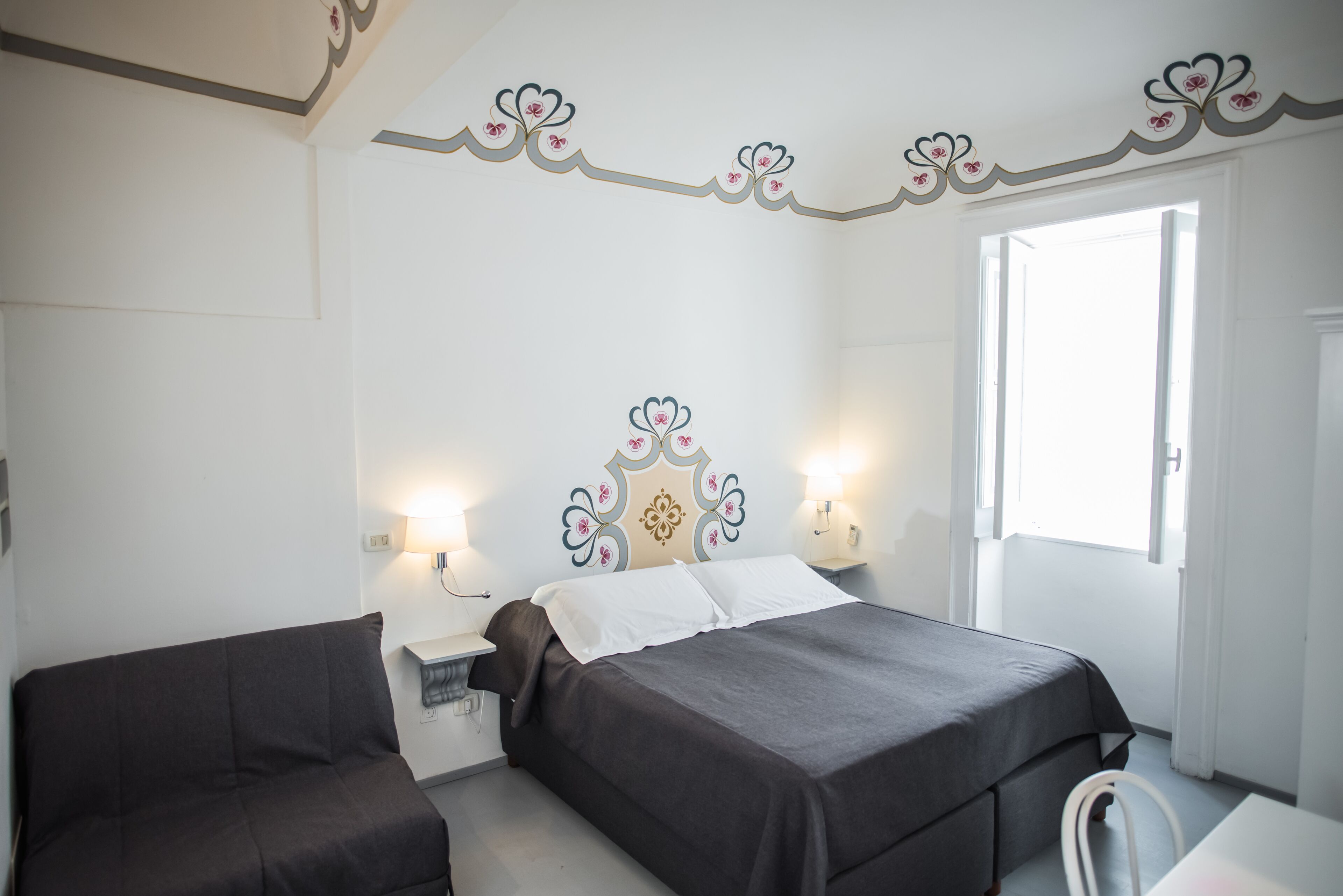 Ein Hotelzimmer mit zwei Betten, einem Schlafsofa, einem Nachttisch und einem Fenster.