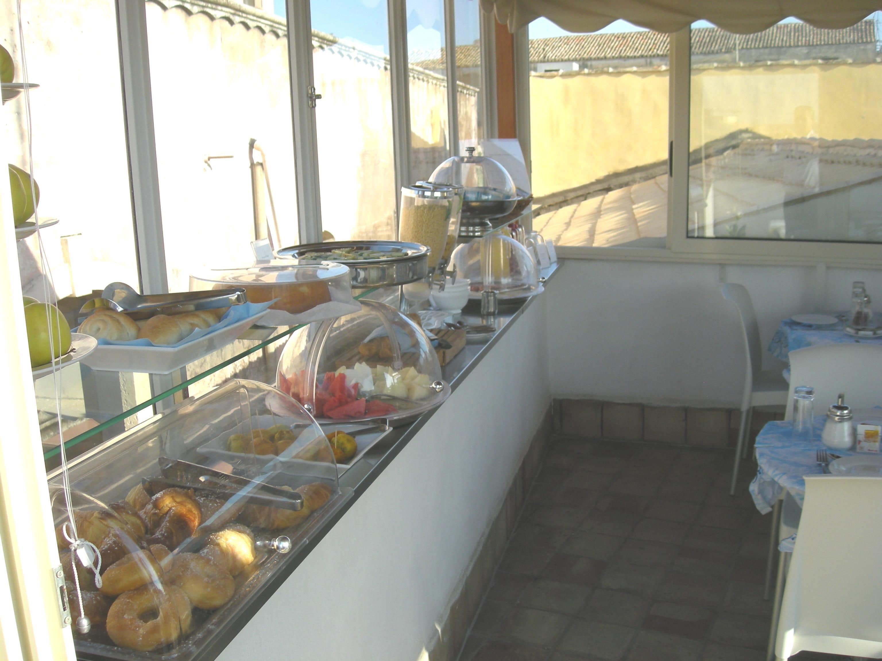A buffet with various food items, including pastries and fruits, in a sunny outdoor setting.