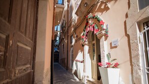 A narrow street with a building on the right featuring a large white planter with red flowers. - Aretusa Vacanze B&B (Syracuse)