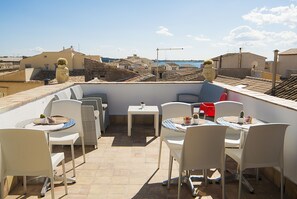 A rooftop terrace with white chairs and tables, a small table with a cactus, and a view of the cityscape.