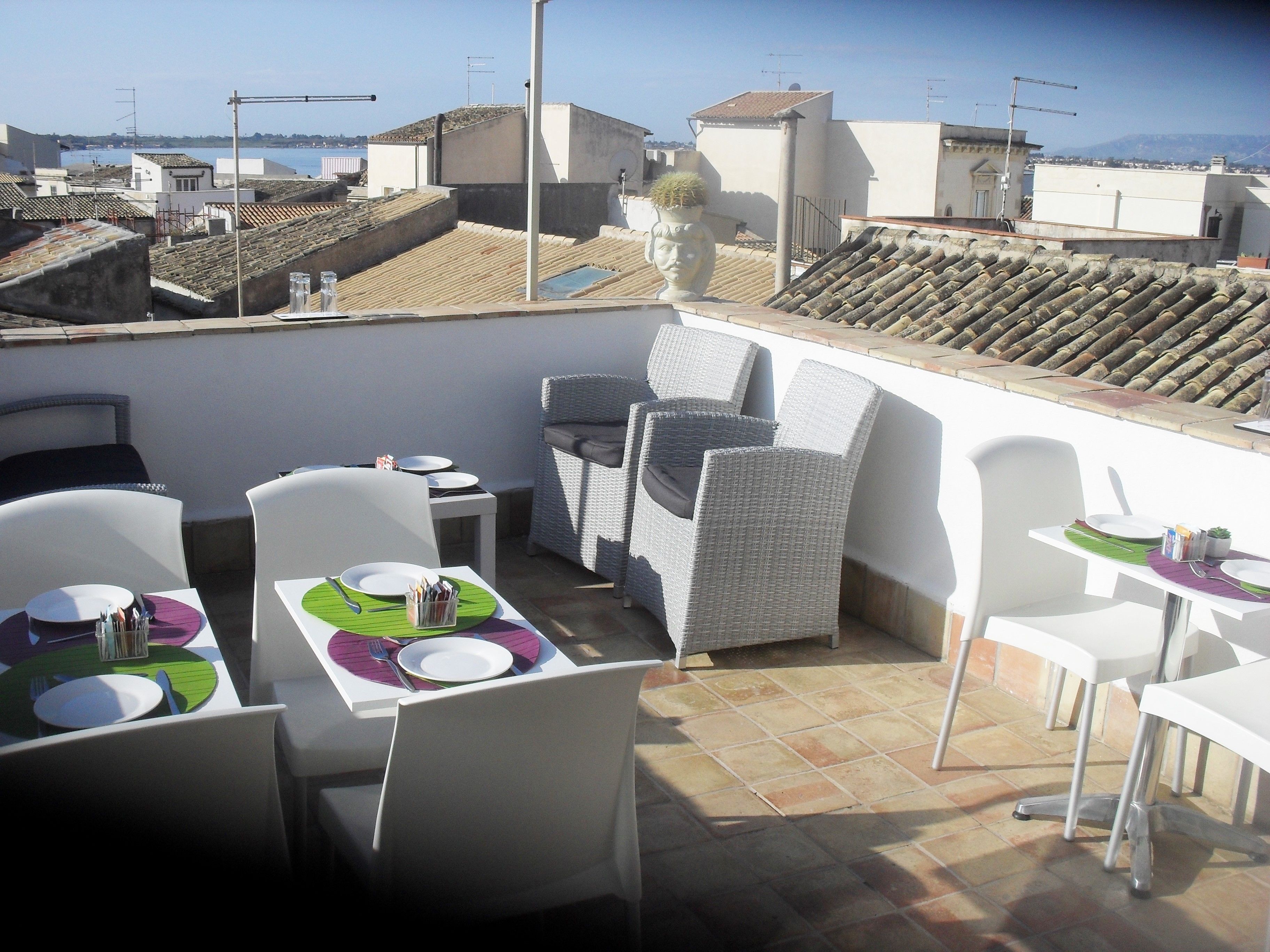A rooftop terrace with outdoor seating, including white chairs and tables, and a view of the cityscape.