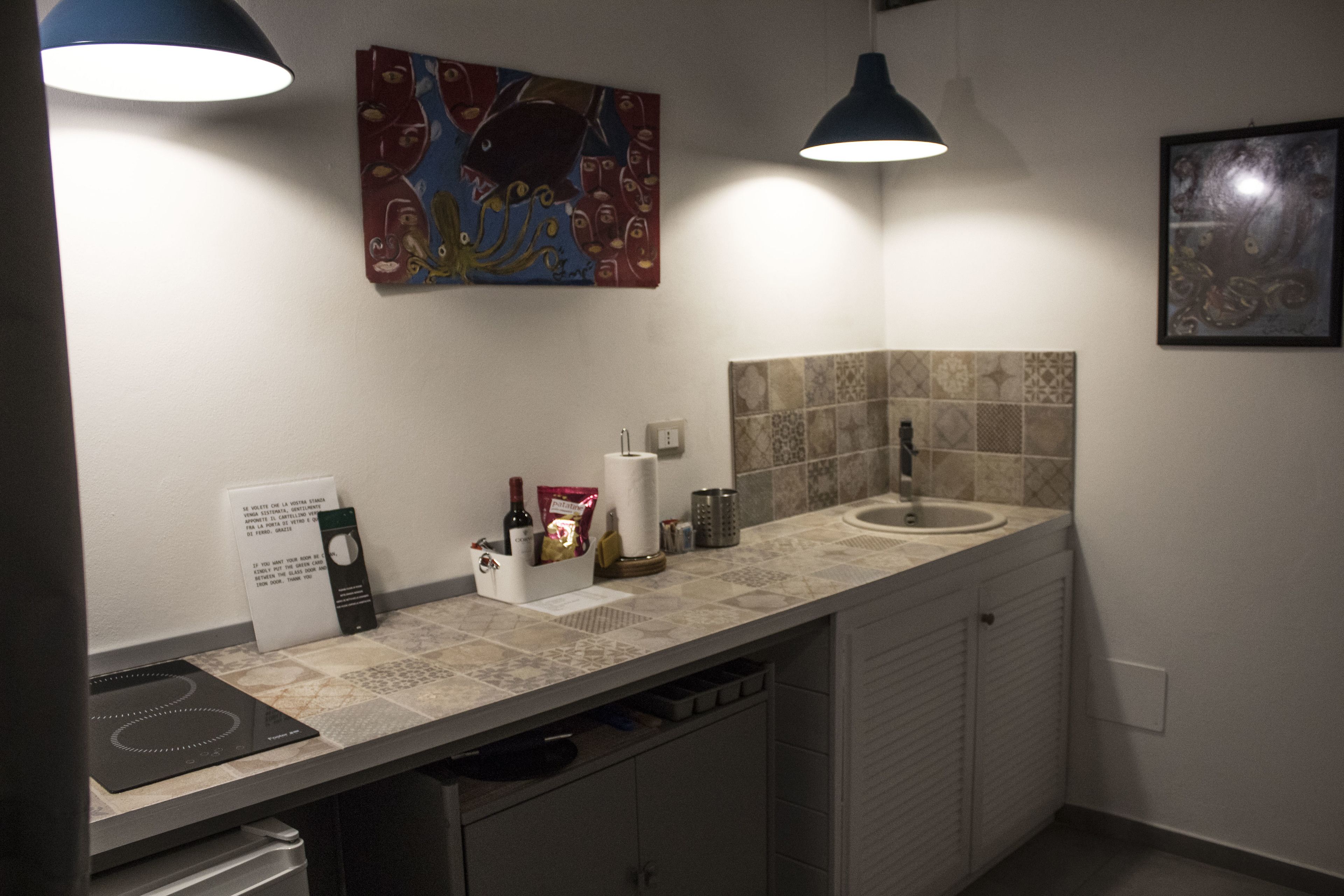 A modern kitchen with a countertop, sink, and cabinets. There are two pendant lights, a painting on the wall, and a sign with text.