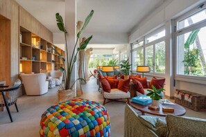 A spacious living area with a large bookshelf, comfortable seating, and a view through large windows. - Hotel le Pleiadi (Forte dei Marmi)