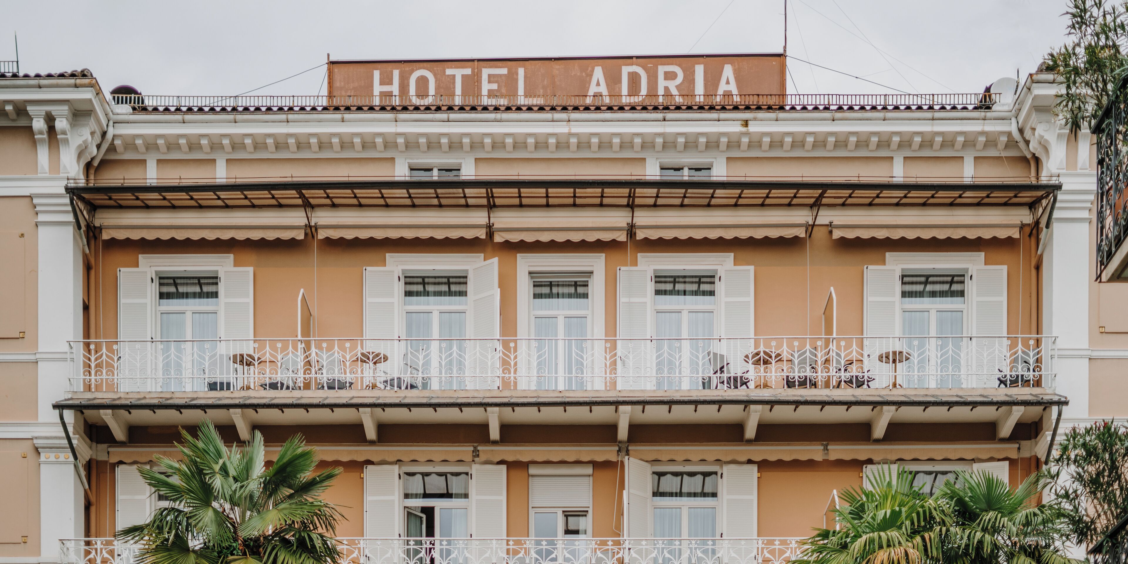 Un hotel con balcón, un cartel que dice 'HOTEL ADRIA' y un estilo arquitectónico tradicional.
