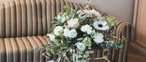 A room with a striped sofa, a glass coffee table with a newspaper, and a vase with flowers.