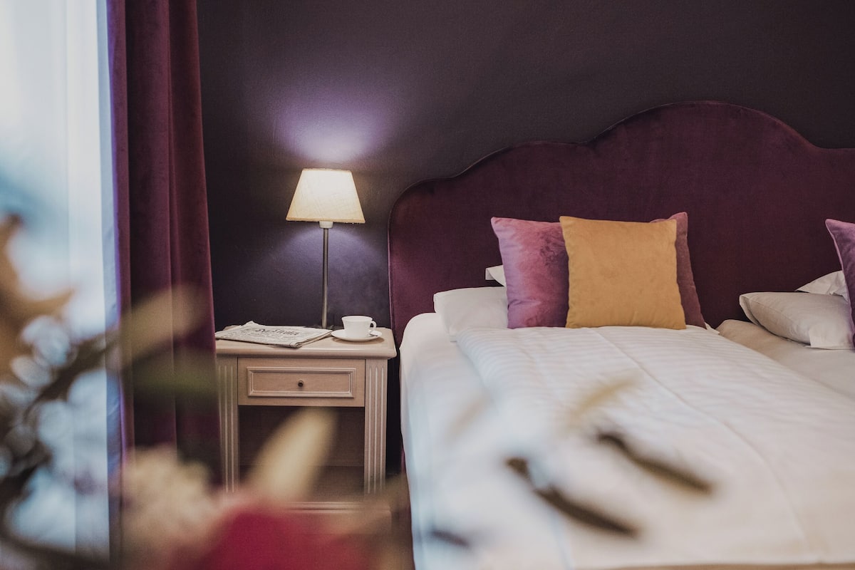 A neatly made bed with a headboard, a bedside table with a lamp, and a cup.