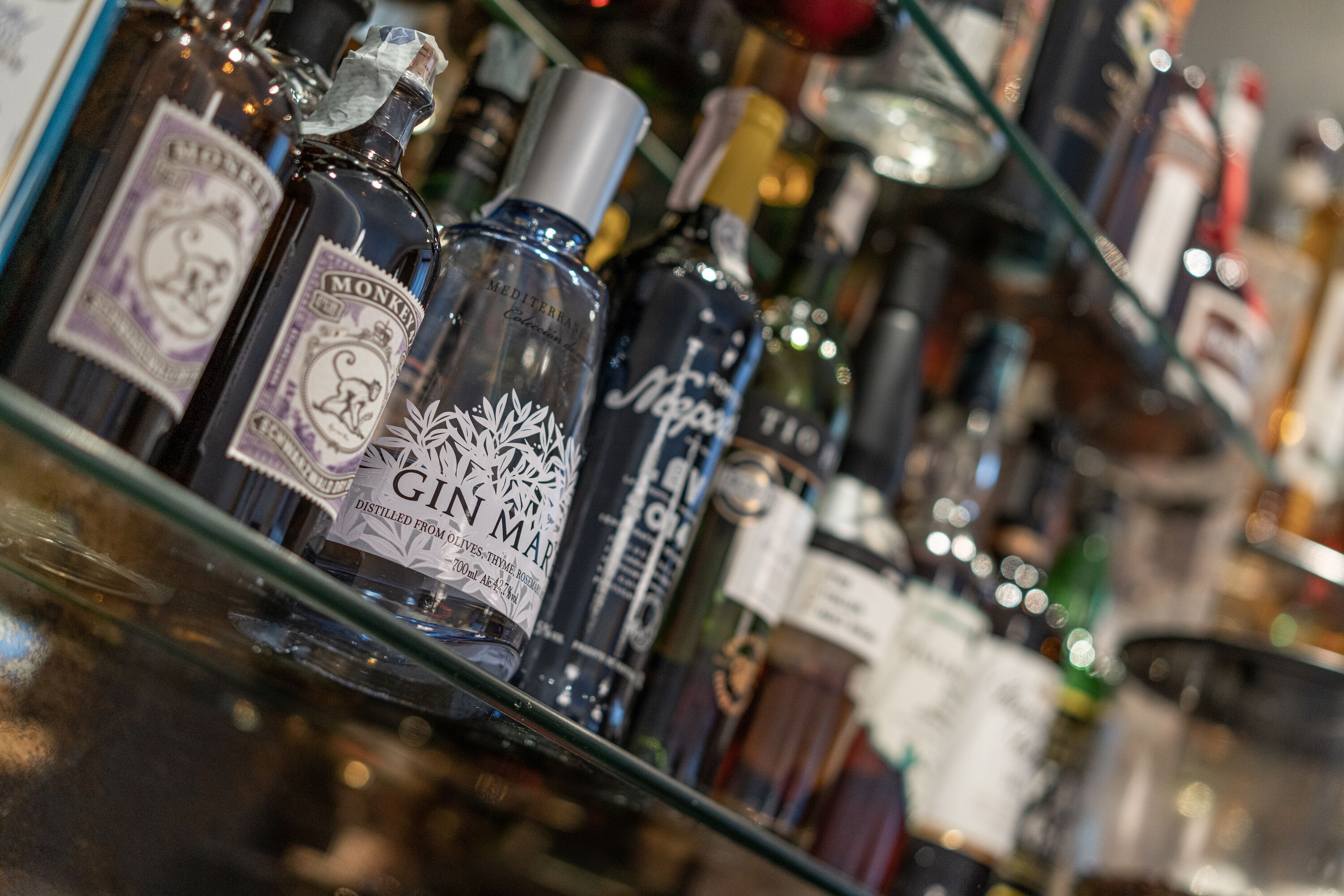 A variety of bottles on a shelf, including a prominently labeled bottle of gin.
