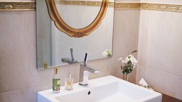 Un baño con un lavamanos blanco, un espejo con marco dorado y una botella de jabón para manos.