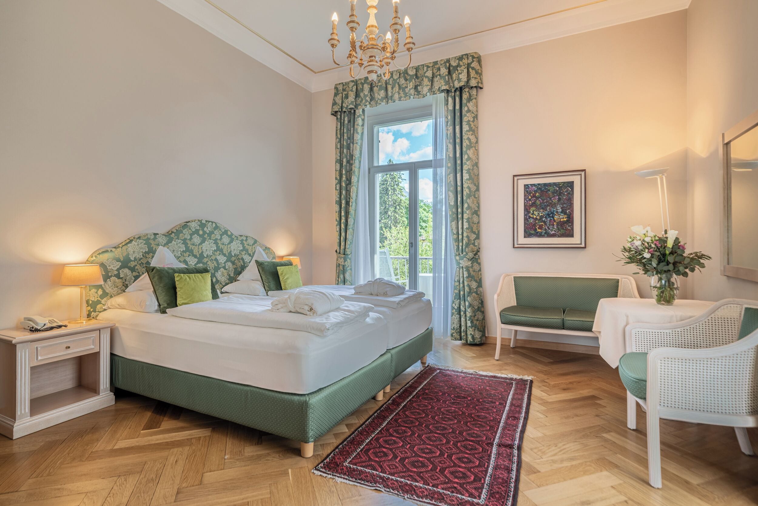 A bedroom with a bed, bedside table, lamp, chair, and a view of the outdoors.