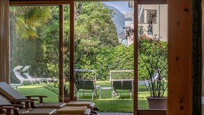 Une chambre avec vue sur un jardin, un espace extérieur aménagé pour s’asseoir et une montagne en arrière-plan.