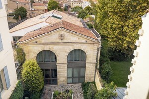 Un edificio de fachada de piedra, ventanas de arco y un pequeño patio con vegetación.