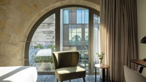 A hotel room with a large arched window, a bed, a chair, a small table with a plant, and a lamp. - La Maison Bord'eaux (Bordeaux)