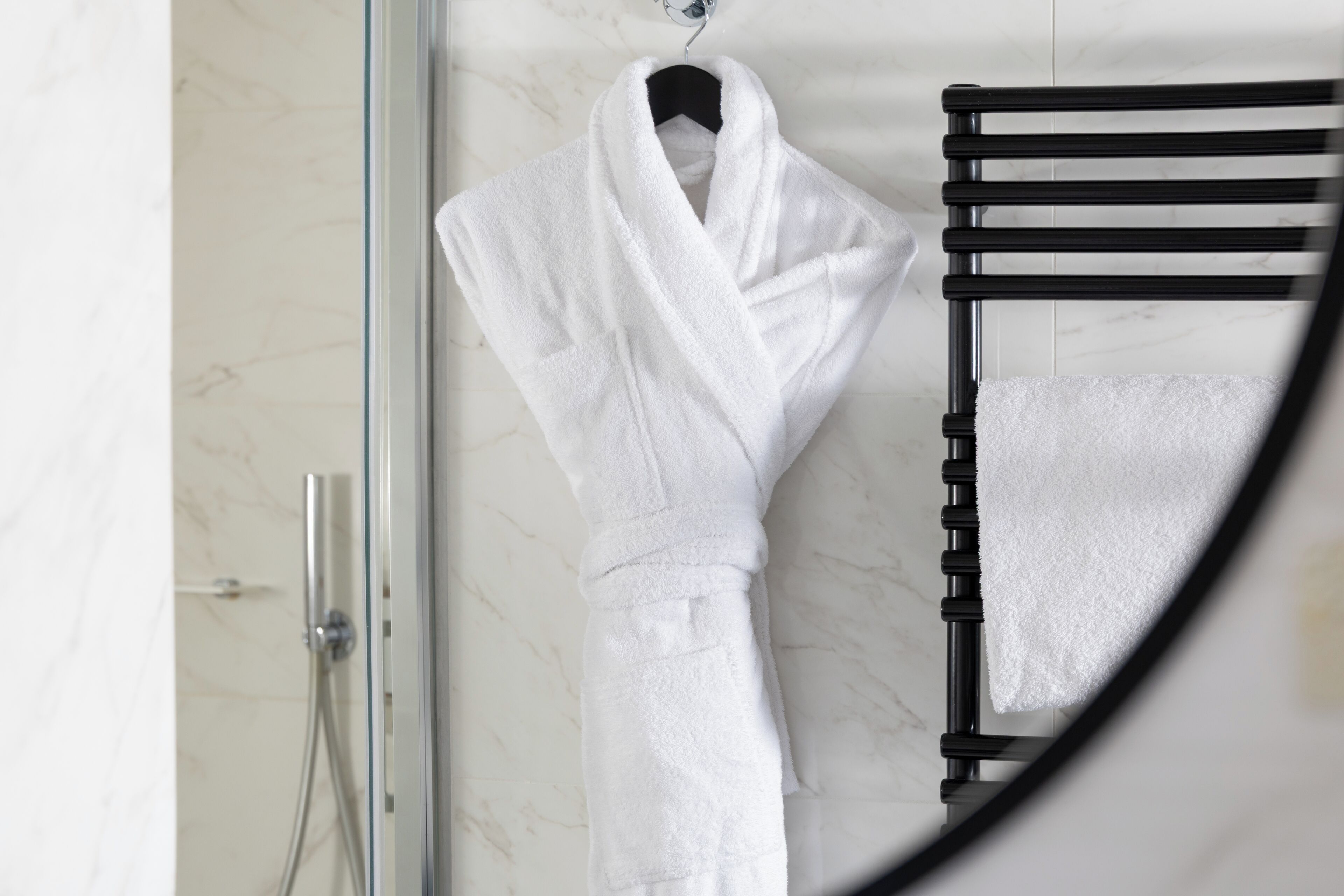 A white bathrobe hanging on a black towel rack in a bathroom with a marble wall.