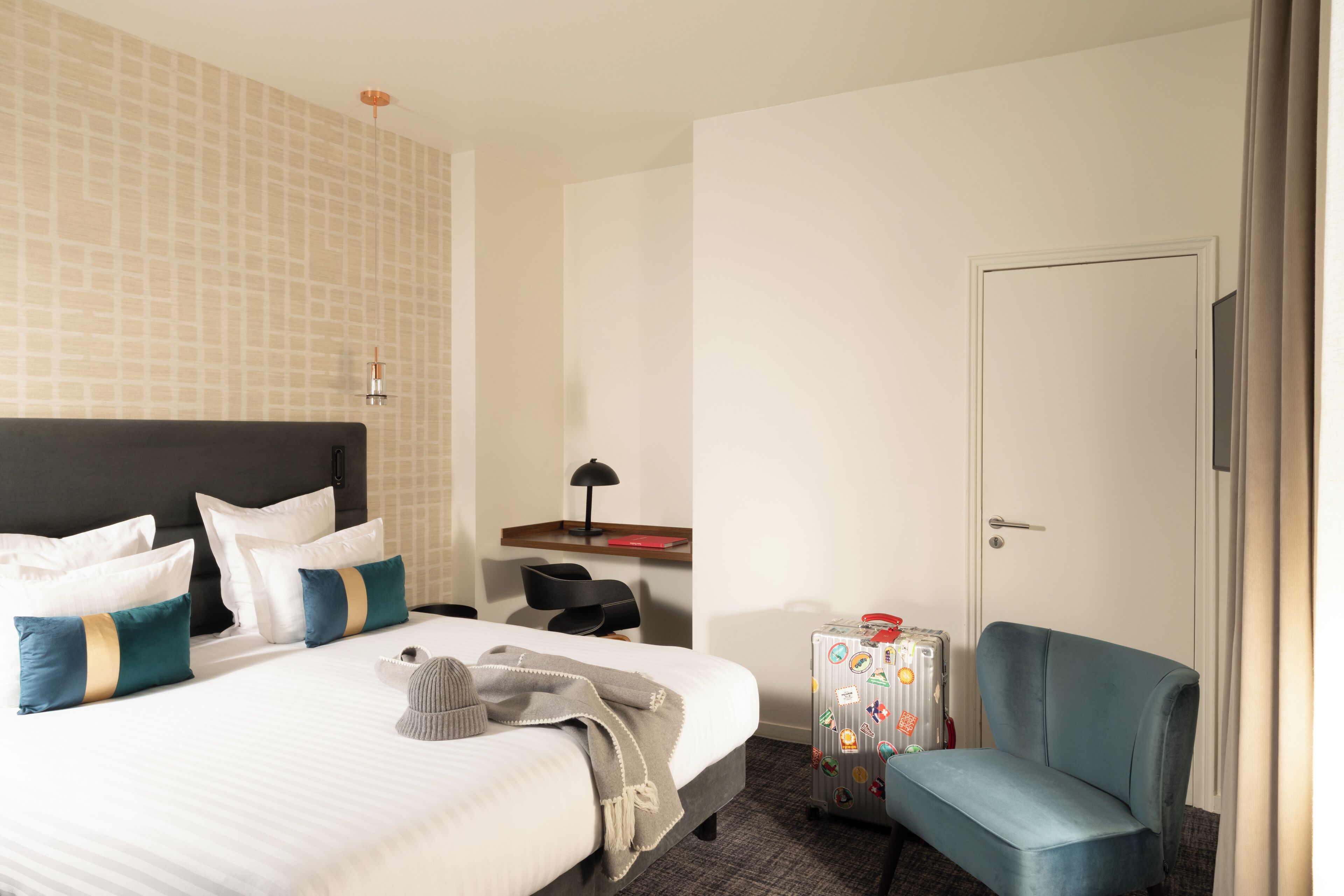Una habitación de hotel con una cama, un escritorio, una silla, una maleta y una puerta.