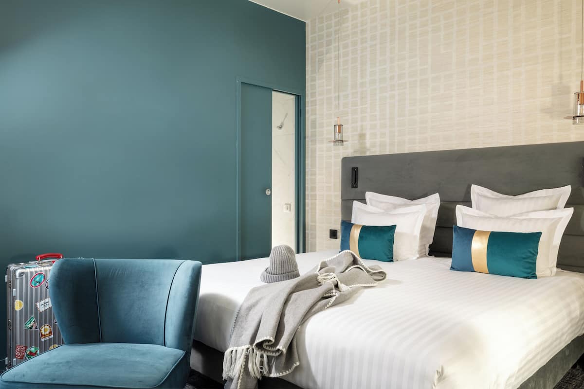 A hotel room with a bed, a chair, and a suitcase.