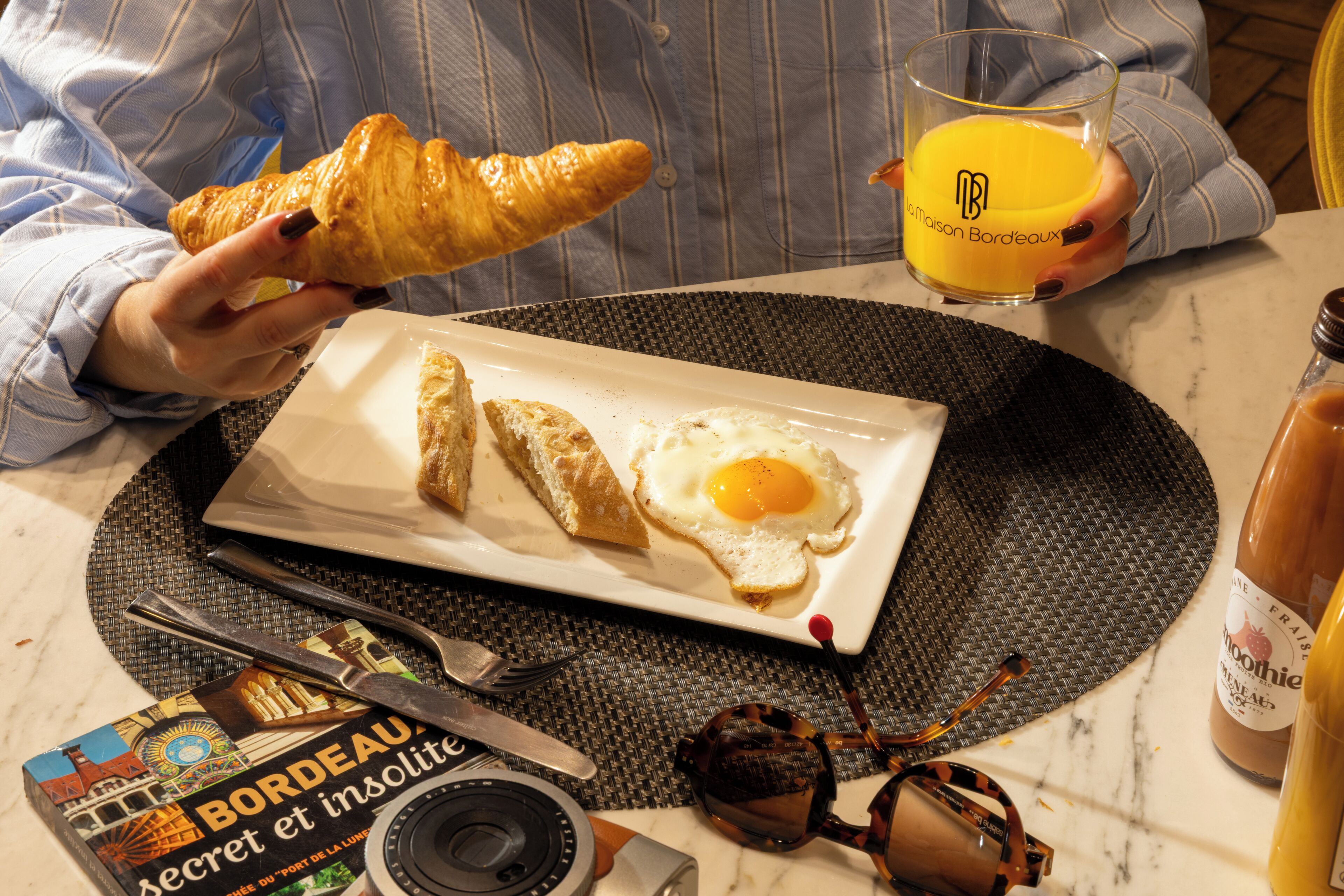 Un desayuno con cruasanes, un huevo frito y un vaso de zumo de naranja en un plato.