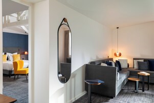 Una camera d'albergo moderna con un divano grigio, un piccolo tavolino in legno, uno specchio e una poltrona gialla.
