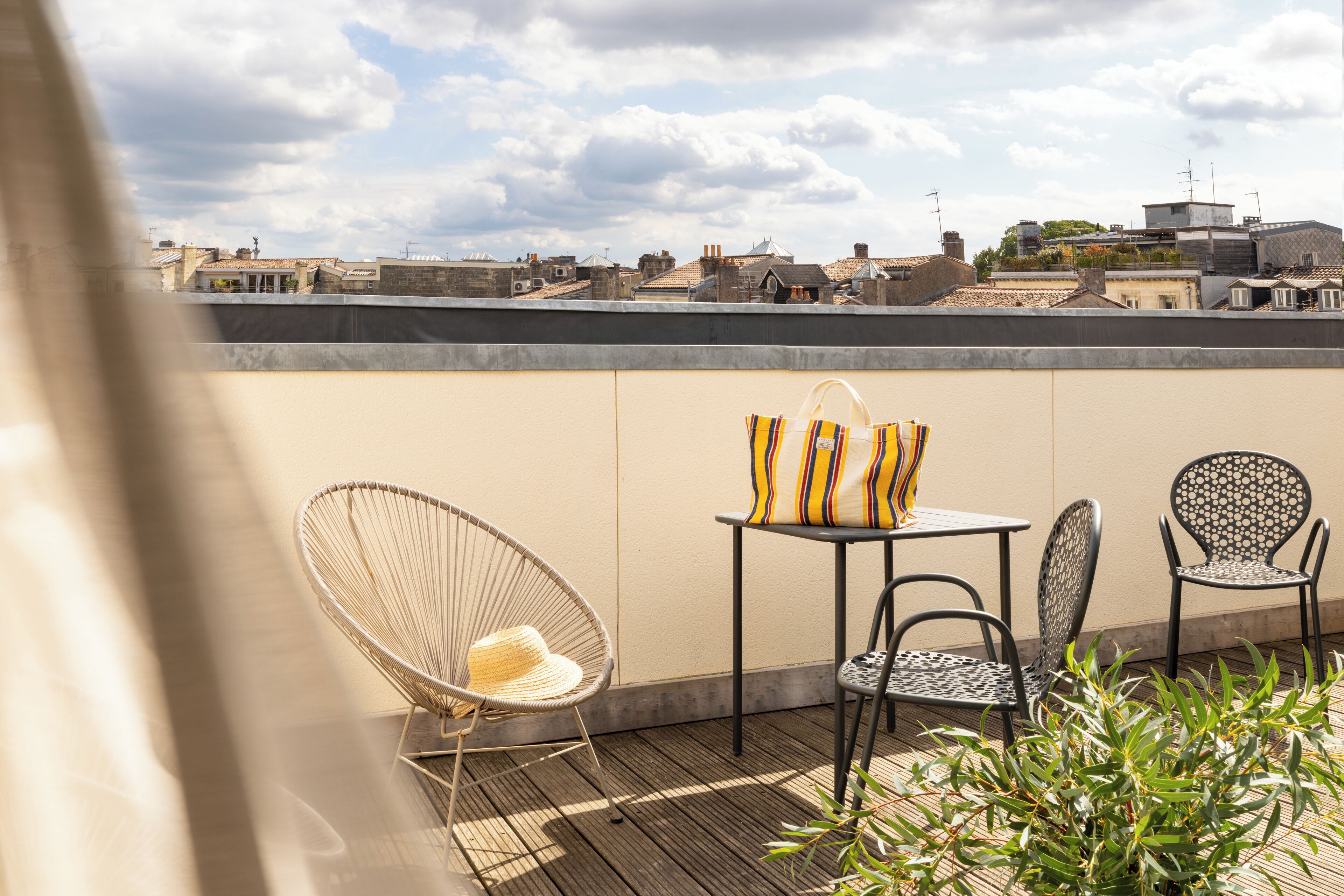 Una terraza en la azotea con una silla de mimbre, una mesita con cojín a rayas y dos sillas estampadas.
