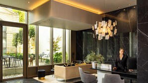 A modern reception area with a sofa, two chairs, a desk, and a large window offering a view of the outdoors. - La Maison Bord'eaux (Bordeaux)