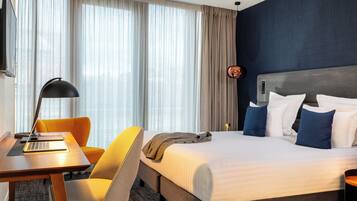 A hotel room with a bed, a desk, a chair, and a lamp.