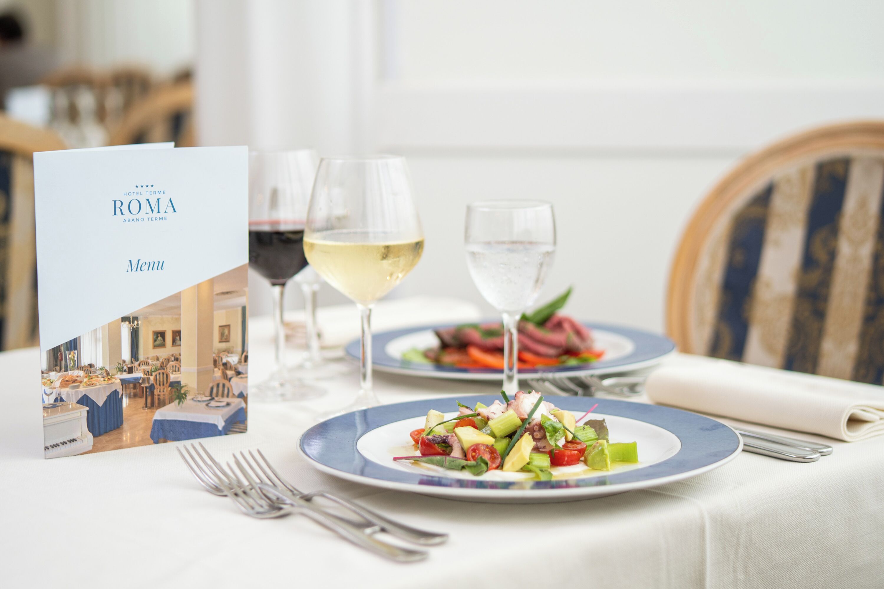 Un tavolo da pranzo imbandito con piatti di cibo, bicchieri di vino e un menu.