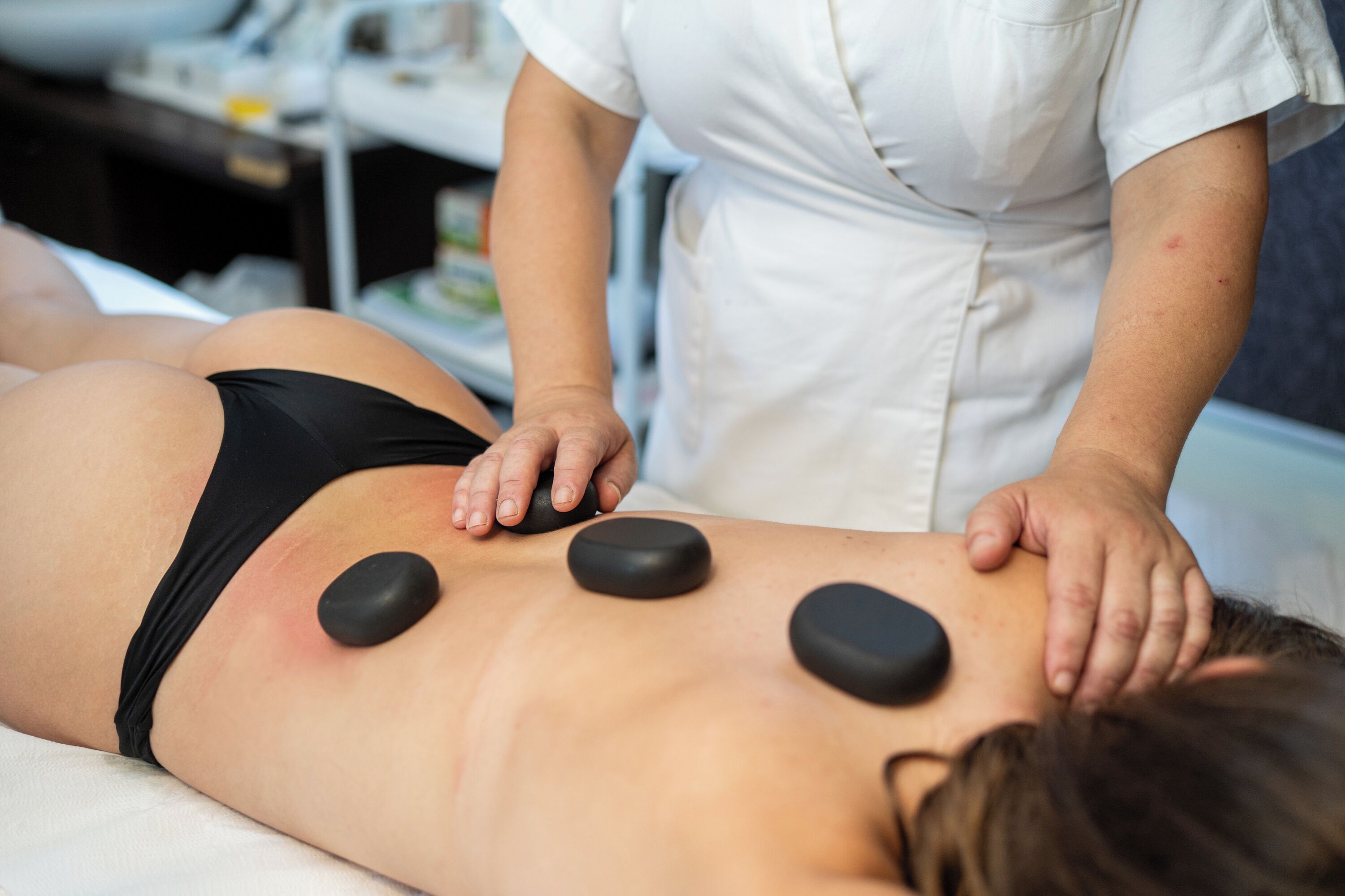 Seduta di massoterapia con un cliente sdraiato a faccia in giù e un terapista che utilizza dei sassi sulla schiena.