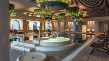 Een modern binnenzwembad met een centraal gelegen hottub, zitgedeeltes en beplanting.