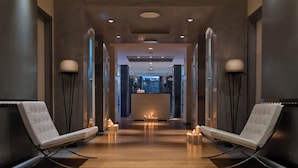 Un moderno vestíbulo de hotel con un mostrador de recepción central, dos sillones y una fila de velas en el suelo.