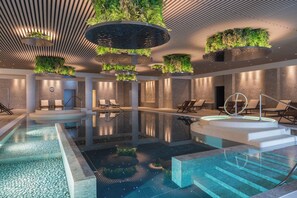 A modern indoor pool area with multiple seating areas and a central water feature.