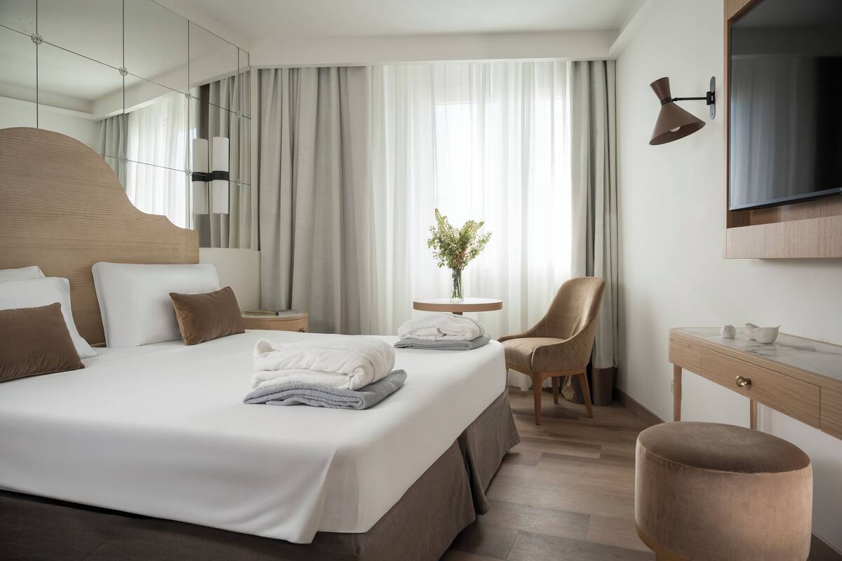 A modern hotel room with a large bed, a desk, a chair, and a TV mounted on the wall.