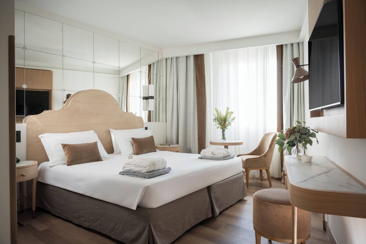A modern hotel room with a large bed, bedside tables, a desk, and a TV.