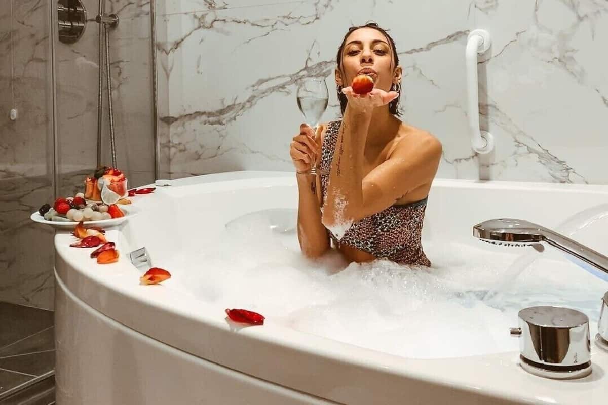 Une personne dans une baignoire, un verre d’eau à portée de main, entourée de pétales de rose.