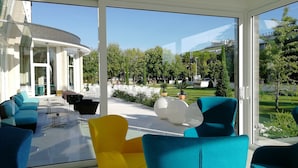 Un espace extérieur moderne, aménagé avec des chaises bleues et jaunes, une table en verre et offrant une vue sur un hôtel et un jardin.