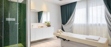 A modern bathroom with a glass shower enclosure, a white vanity, and a massage table.