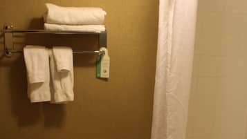 A bathroom with a toilet, a towel rack with folded towels, a toilet paper holder, and a bathtub with a shower curtain.