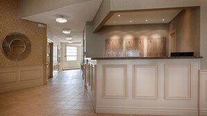 Un hall spacieux doté d’un îlot central comprenant un évier et un plan de travail intégrés, flanqué de meubles en bois et d’un grand miroir.