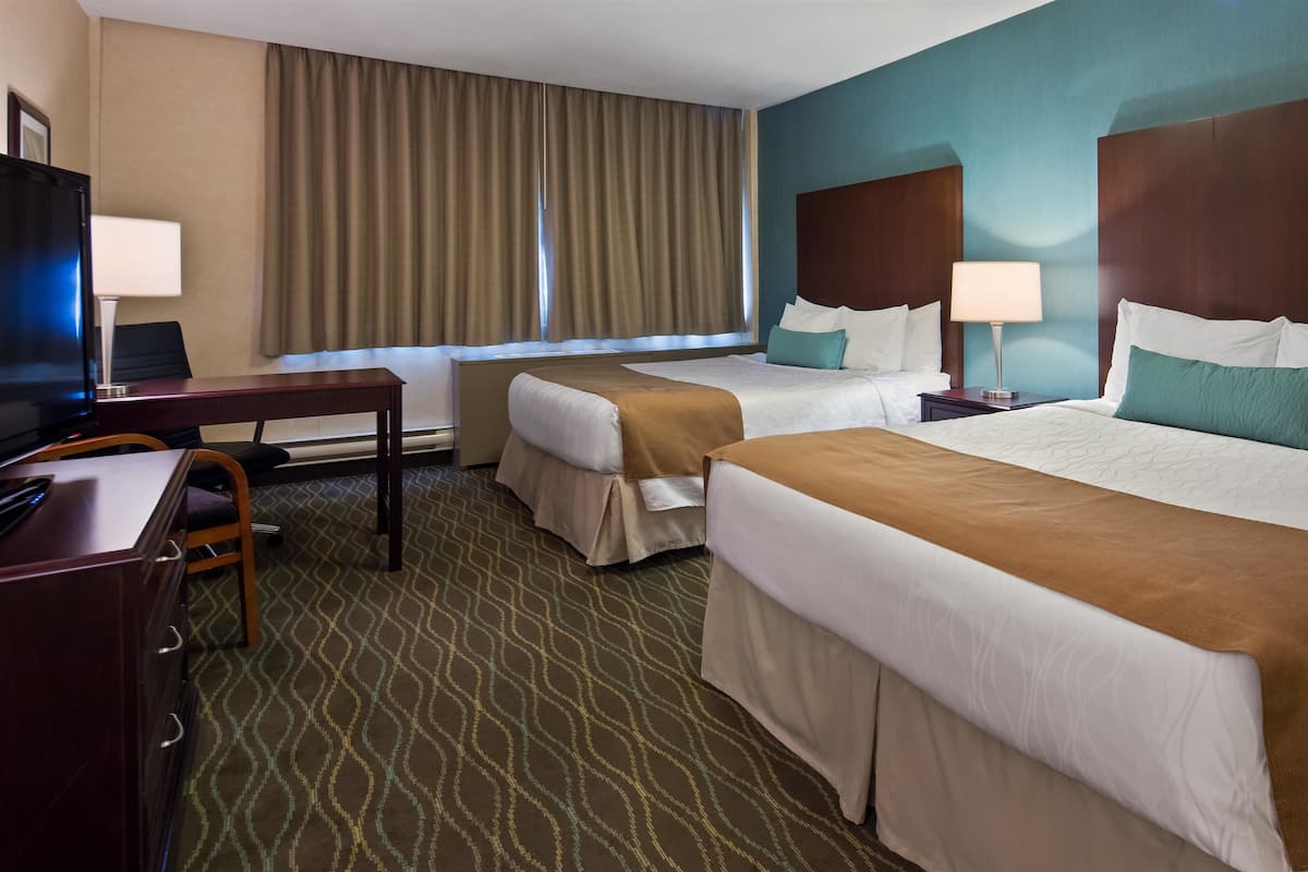 A hotel room with two beds, a desk, a TV, and a window with curtains.
