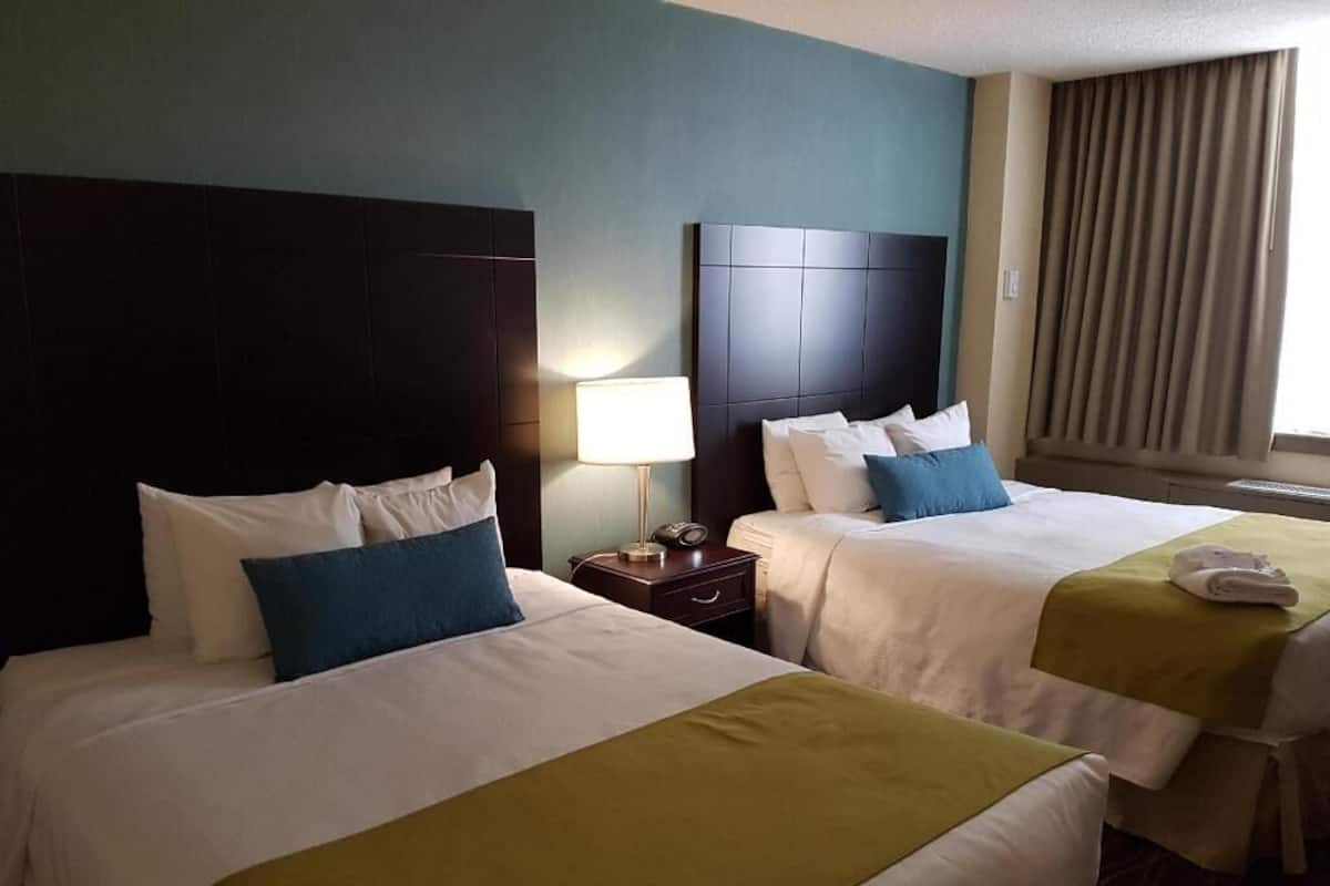 A hotel room with two beds, a nightstand, a lamp, and a window with curtains.