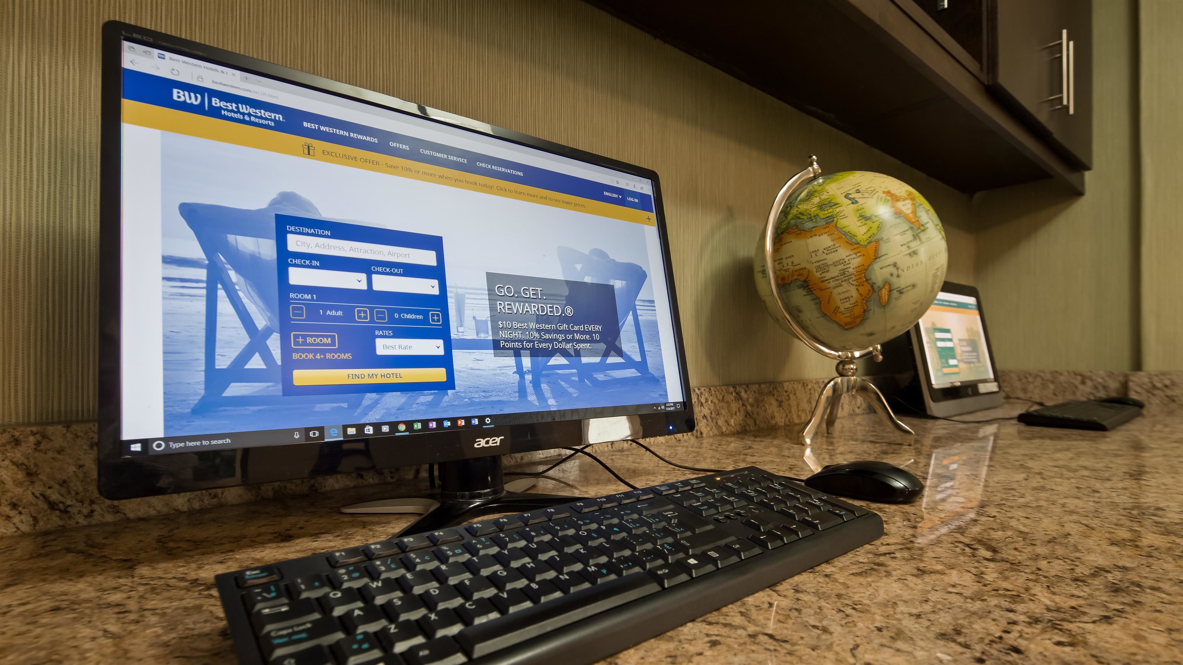 Un monitor che mostra un sito web per prenotare un hotel, una tastiera, un mouse e un mappamondo su una scrivania.