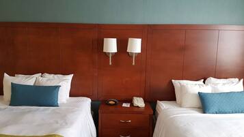A hotel room with two beds, each with white bedding and blue pillows, a wooden headboard, a nightstand with a lamp, and a telephone.